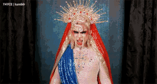 a drag queen with a crown on her head and a blue and gold robe