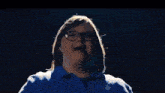 a young boy wearing glasses and a blue shirt is making a heart with his hands .