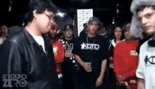 a group of people are standing in a room and one of them is wearing a shirt that says kotd on it .