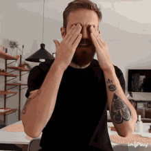 a man with a tattoo on his arm covering his eyes with his hands