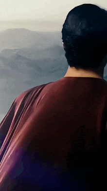 a man wearing a red cape looks out over a cloudy sky