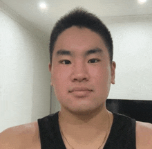 a man wearing a black tank top and a gold chain around his neck looks at the camera