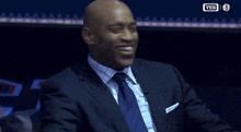 a man in a blue suit and tie is smiling in front of a yes logo
