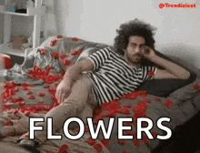 a man in a striped shirt is laying on a bed covered in rose petals and the word flowers is above him