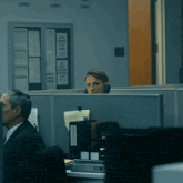 a man sits in an office cubicle with a binder labeled " aaoc " on it