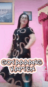 a woman in a black dress is standing in front of a pink wall and a pink curtain .