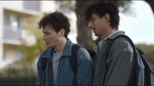 two young men with backpacks stand next to each other