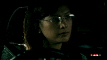 a woman wearing glasses is sitting in a car with a blurred background that says full