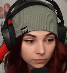a woman wearing headphones and a beanie has a label on her beanie that says ' established in ' on it