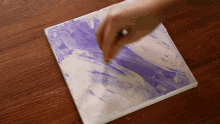 a person is painting a picture on a canvas with purple and white paint