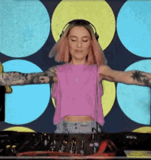 a woman wearing headphones and a pink crop top is playing music
