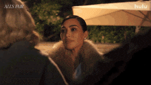 a woman in a fur coat talks to two other women in front of a sign that says all 's fair on it