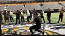 a man is kneeling down on a football field with a group of people standing behind him .