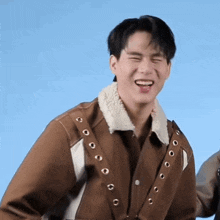 a man in a brown jacket is laughing with his eyes closed .
