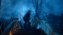 a man in a hat is standing on a bridge in the dark holding a bag .