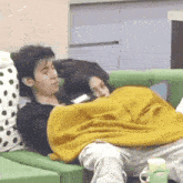 a man and a woman are laying on a green couch with a yellow blanket .