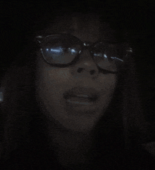 a woman wearing glasses is making a funny face in the dark