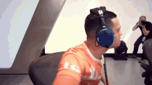 a man wearing headphones and an orange shirt with the letter r on the sleeve