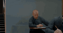 a man sitting at a desk giving the middle finger to another man