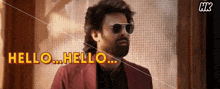 a man wearing sunglasses and a suit says hello
