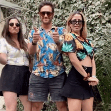 a man and two women are posing for a picture and the man is wearing a hawaiian shirt