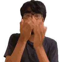 a man with glasses and a black shirt is covering his face with his hands