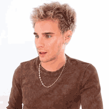 a young man wearing a brown shirt and a gold chain necklace