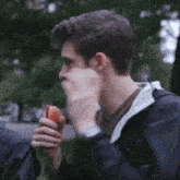 a man in a black jacket is eating a hot dog in a park