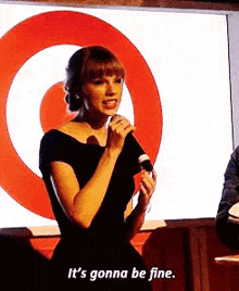 a woman is holding a microphone in front of a target logo and saying `` it 's gonna be fine '' .