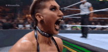 a woman is screaming in a wrestling ring while a referee watches .