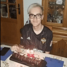 a man in a miguel shirt sits at a table with a cake on it