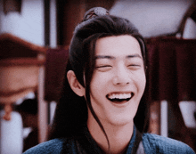 a young man with long hair is laughing with his eyes closed and his mouth open .