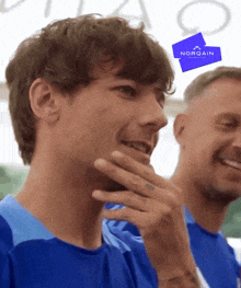 a man in a blue shirt is smiling next to another man with a norqain sign above them