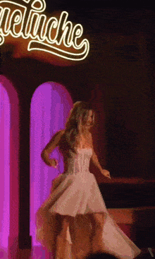 a woman in a white dress is dancing in front of a sign that says " angeliche "
