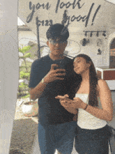 a man and a woman are taking a selfie in front of a sign that says " you look good "