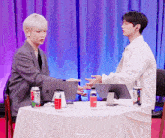 two men are sitting at a table with a can of soda and a bottle of water on it