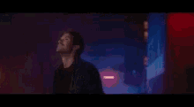 a man in a black jacket is standing in a dark room looking up .