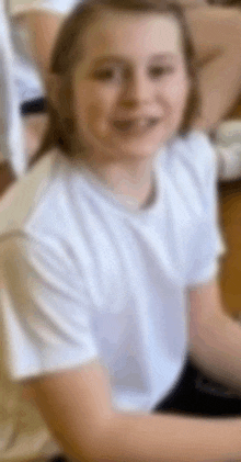 a young girl wearing a white shirt is sitting on the floor and smiling .