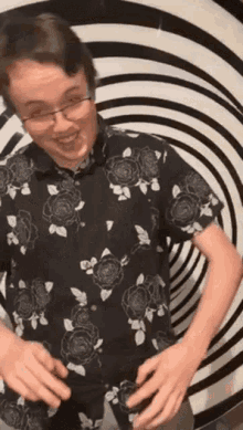 a young man wearing glasses and a black and white floral shirt is standing in front of a hypnotic background .