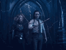 a man and a woman are standing next to each other in a dark room holding a sword .