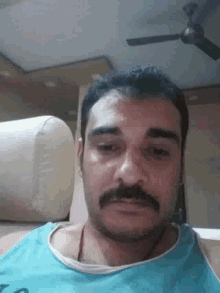 a man with a beard and mustache is standing in front of a ceiling fan and a couch .