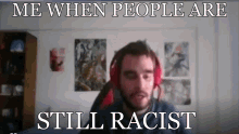 a man wearing red headphones is sitting in front of a wall with posters on it and says me when people are still racist