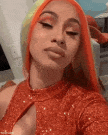 cardi b is wearing a red dress and orange hair .