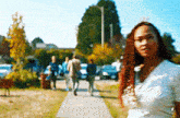 a woman is standing on a sidewalk in front of a group of people walking down a sidewalk .