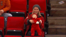 a woman is holding a baby in a stadium sponsored by nhlcane