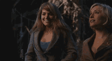 two women are standing next to each other in a dark room and one of them is taking off her jacket