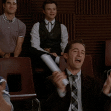 a man in a striped shirt applauds while another man in a suit holds a microphone