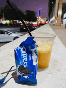 a bag of oreo cookies next to a cup of orange juice with a straw