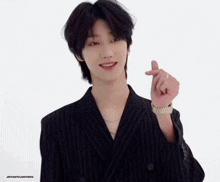 a man in a black suit is making a heart with his hand