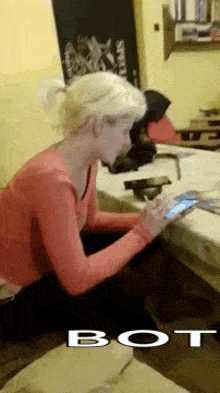a woman in a red shirt is sitting at a table using a cell phone .